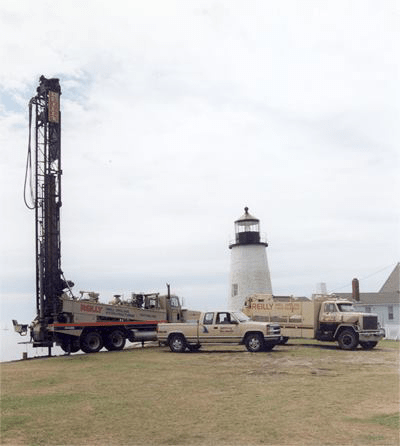 (from left to right) A drilling truck, a pickup truck, and a semi-trailer truck parked in front of a lighthouse