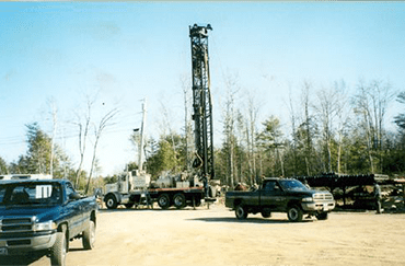 A well-drilling truck on a desert plain next to a forest